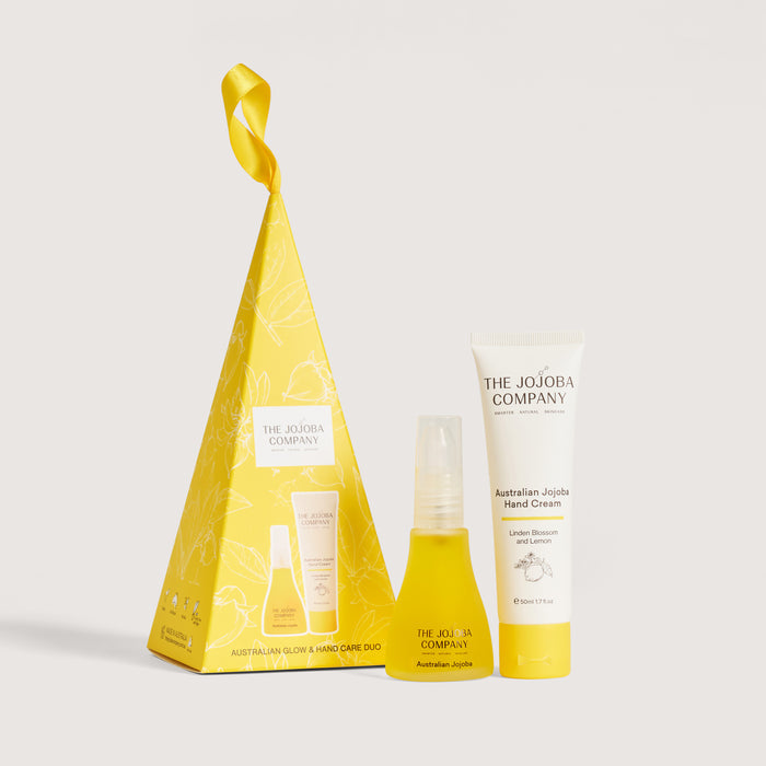 The Jojoba Company Australian Jojoba Hand Cream gift set, featuring a yellow pyramid-shaped box with a ribbon loop, a yellow bottle, and a white hand cream tube on a light gray background.