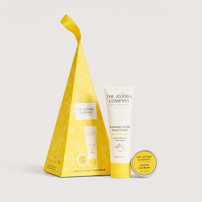 The Jojoba Company Australian Jojoba Hand Cream and Jojoba Lip Balm set, featuring a yellow gift bag, a white and yellow hand cream tube, and a round yellow lip balm tin on a light gray background.