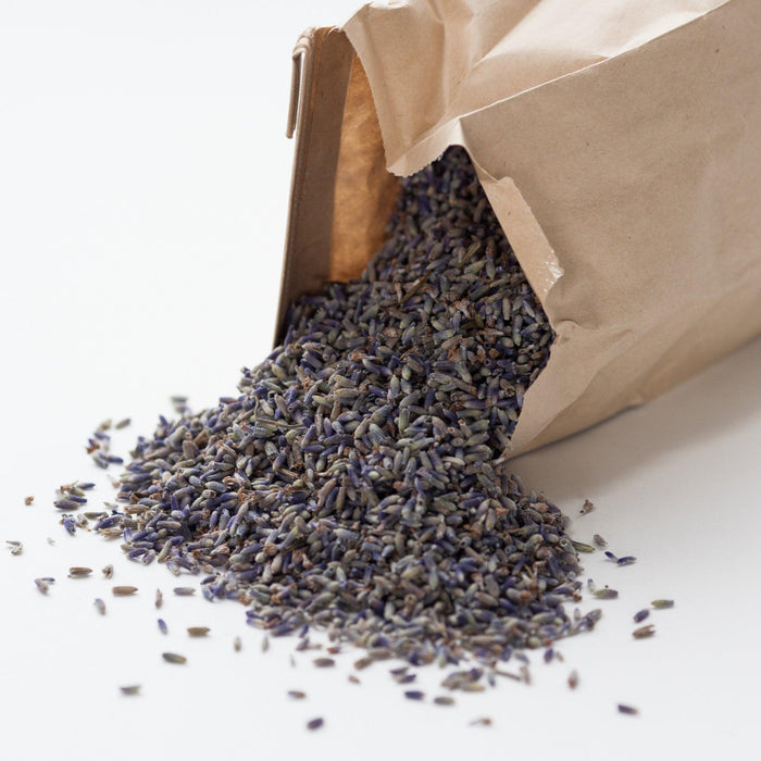 A brown paper bag with loose  lavender spilling out onto a white surface. The lavender buds are light purple color.