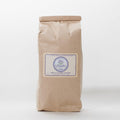 A closed brown paper bag filled with dried French lavender flowers. The bag has a label that says "Lavender by the Bay" and "Dried Lavender Flowers.