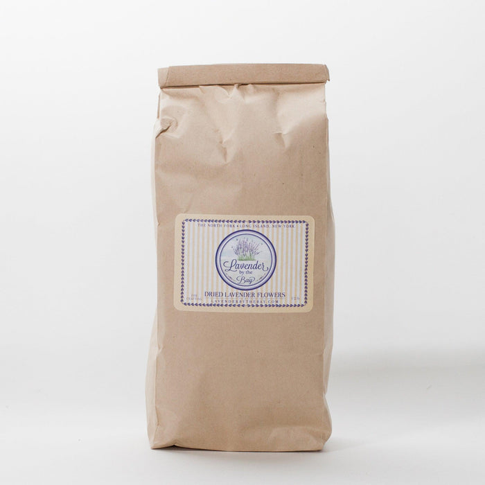 A closed brown paper bag filled with dried French lavender flowers. The bag has a label that says "Lavender by the Bay" and "Dried Lavender Flowers.
